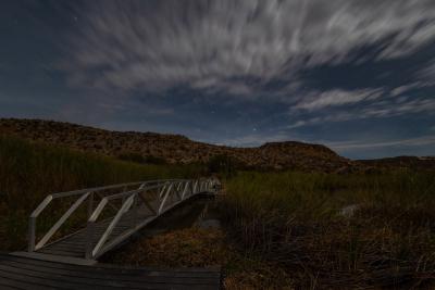 A bridge over the Rio Grande marsh under a cloudy night sky