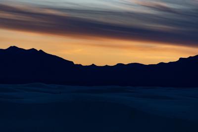 Sunset behind the mountains with dark sand dunes in the foreground