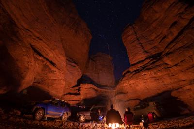 Three people sitting in front of a campfire in a canyon