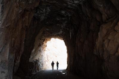 Two people walking through a dark tunnel with light in the distance